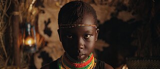 Close up of a brown skinned girl with beads around her neck looking defiant