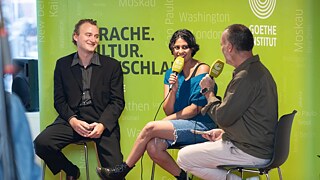 Iven Yorick Fenker and Sonali Beher in conversation with Vladimir Balzer on stage, in front of a green Goethe-Institut backdrop