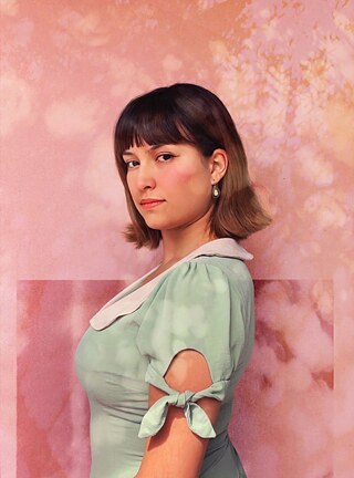 A foto mostra Beatriz Brajal fotografada de perfil, olhando para a câmara diante de uma parede pintada de rosa.