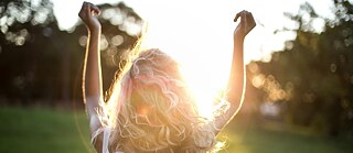 Ein Mädchen von hinten streckt die Arme in die Luft