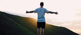 Ein Mann steht auf einem Berg und hat die Arme ausgebreitet.