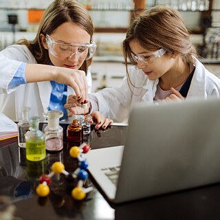 Eine Chemiestudentin und ihre Professorin führen im Labor ein Experiment durch. Sie tragen Schutzbrillen.