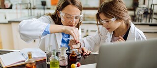 Una estudiante de química y su profesora están realizando un experimento en el laboratorio. Ambas llevan gafas de protección.