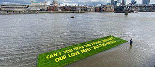 Large green sign made from grass floating on the Thames river