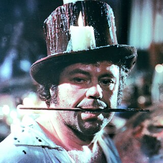 Colour close up of an oder man wearing a tall hat with a burning candele on its rim