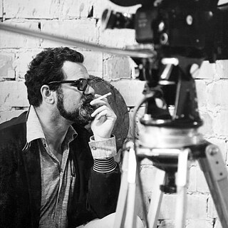 Black and white image of a white man in profile next to a film camera