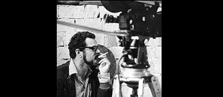 Black and white image of a white man in profile next to a film camera