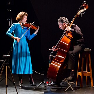 Eine Geigenspielerin im blauen Kleid und ein Cellist spielen konzertriert und energisch im Duett. 