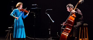 Eine Geigenspielerin im blauen Kleid und ein Cellist spielen konzertriert und energisch im Duett. 