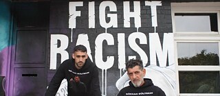 L'image montre 2 personnes devant un tag qui dit "Fight racism"