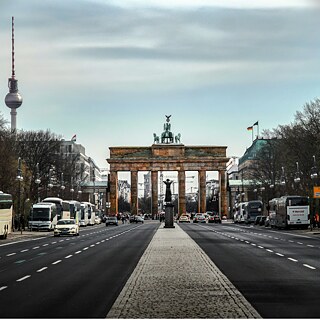 Straßenansicht des Brandenburger Tors in Berlin mit leichtem Verkehr und dem Fernsehturm im Hintergrund.