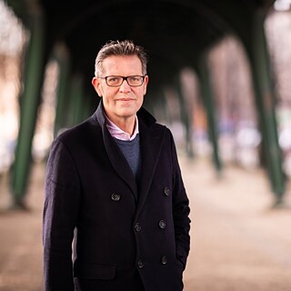 Der Soziologe Steffen Mau steht unter einer Brücke mit grünen Brückenpfeilern.