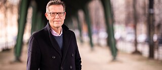 Der Soziologe Steffen Mau steht unter einer Brücke mit grünen Brückenpfeilern.