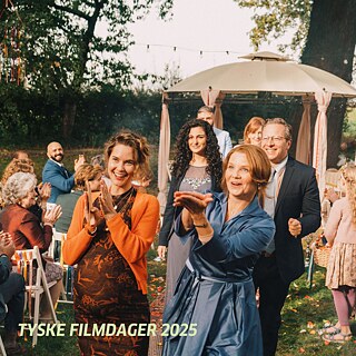 Gruppe von Menschen bei einer Feier im Freien, mit Stühlen, Dekoration und einem Pavillon im Hintergrund. 