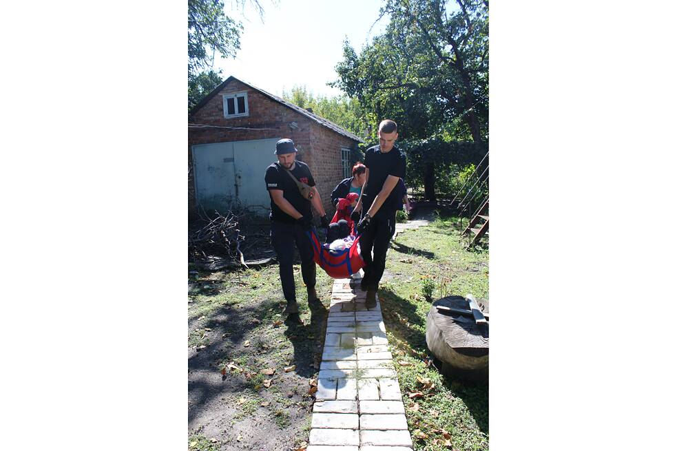 Pomocníci Roman Buhajov (vlevo) a Eduard Skoryk nesou Ljudmilu Ivanivnu z jejího domu v Kramatorsku do evakuačního vozidla.