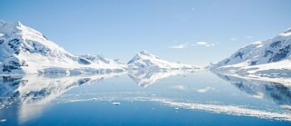 Snow and ice covered mountins surrounding crystal clear water.