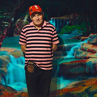 Ein Mann mit einer roten Schirmmütze steht vor einer Tapete mit einem blaugünen Wasserfall im Hintergrund.