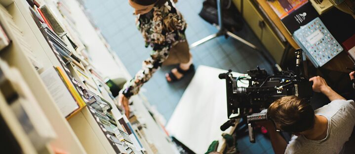 Двоє людей із камерою фільмують жінку перед полицями у книжковому магазині