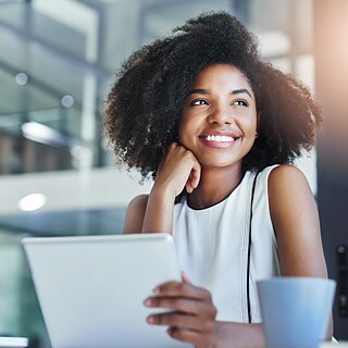 Eine Geschäftsfrau arbeitet im Büro mit Tablet und Laptop. Sie lächelt glücklich.