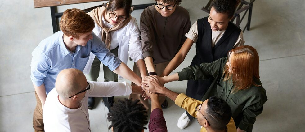 Mehrere Leute stehen im Kreis und halten einander die Hände.