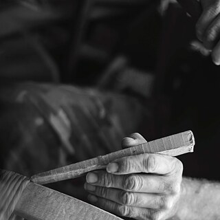 Sandalye yapmakta olan bir kişinin siyah beyaz yakın çekimi. Bu kişi sağ elindeki çekiçle, sol eliyle tuttuğu tahta bir takoza vurmak üzeredir. Resmin üzerinde yeşil ve beyaz harflerle yazılmış şu yazı bulunmaktadır: The Art of Making, Sergi, Fotoğraf ve Metinler, Georgios N. Paparoditis