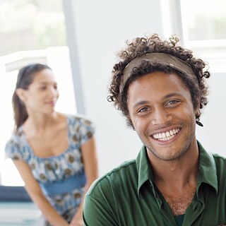 A young man looking cheerfully into the camera. Three other people in the background.