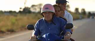 Ein Mann mit Helm fährt ein Motorrad und transportiert dabei zwei Frauen