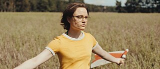 A girl holding two flags is walking through a field.