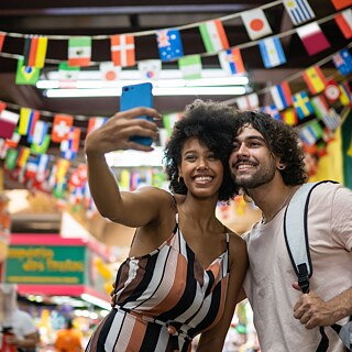 Menschen feiern im Freien, während buntes Konfetti durch die Luft fliegt. Die Sonne scheint hell im Hintergrund und erzeugt eine warme, festliche Stimmung.