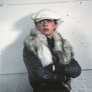 A young white woman with a white cap leaning against a white wall