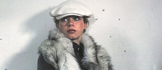 A young white woman with a white cap leaning against a white wall