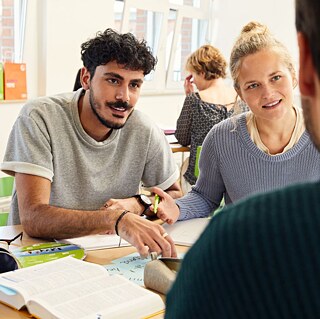 Two students engaged in discussion while sitting at a table in a bright classroom