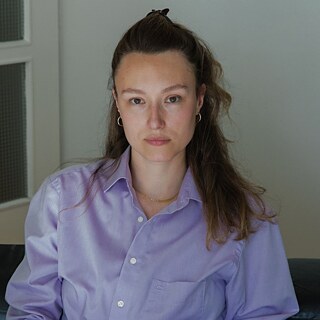 Eine Person in einem hell‑lila Hemd vor einer hellen Wand