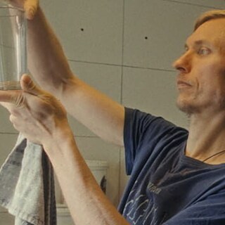 A man holding a glass to see if it's clean. Key image for 'Soldiers of Light' a film at Antenna Festival