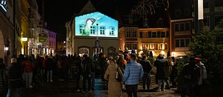 Menschen sehen nachts eine Projektion auf einer Hauswand.