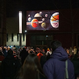 Menschen sehen nachts eine Projektion von Planeten und Monden auf einer Hauswand.