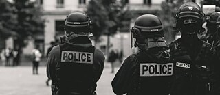 Riotpolice on an empty space. One policeman with facemask looks at us.