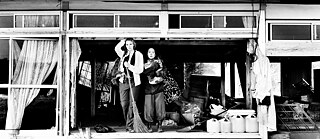 Filmstill aus Grüße aus Fukushima: Zwei Frauen schauen aus der Eingangstür eines verfallenen japanischen Hauses.