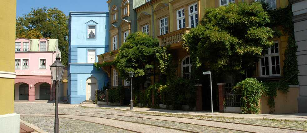 Blick auf einen Straßenzug mit gelben, babyblauen und rosanen Altbauhäusern auf dem Filmgelände der Bavaria Filmstadt. 