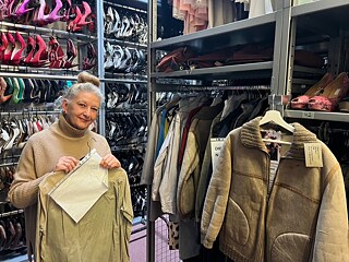 Eva Scherrer, Leiterin des Kostümverleihs, steht vor einem Regal mit High Heels in verschiedenen Farben und hält ein Kleidungsstück in die Kamera.