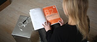 Blick von oben auf eine Deutschlehrerin, die eine Goethe-Prüfung B2 in der Hand hält.