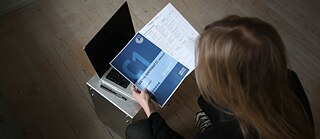 Blick von oben auf eine Deutschlehrerin, die eine Goethe-Prüfung C1 in der Hand hält.