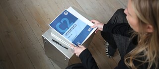 Blick von oben auf eine Deutschlehrerin, die eine Goetheprüfung C2 in der Hand hält.