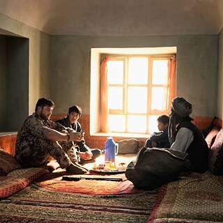 Filmstill aus Zwischen Welten von Feo Aladag. Ein deutscher Soldat sitzt auf einem Teppich im Haus einer afghanischen Familie und unterhält sich mit ihnen.