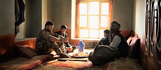 Filmstill aus Zwischen Welten von Feo Aladag. Ein deutscher Soldat sitzt auf einem Teppich im Haus einer afghanischen Familie und unterhält sich mit ihnen.