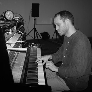 Khaled Kurbeh, a pianist sitting at an upright piano with a serious facial expression on his face