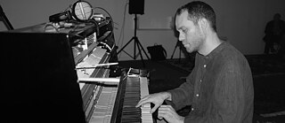 Khaled Kurbeh, a pianist sitting at an upright piano with a serious facial expression on his face