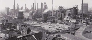 Black and white image of city scape, houses in forefront and backdrop of chimneys