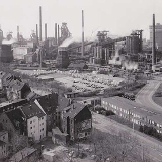 Black and white image of city scape, houses in forefront and backdrop of chimneys