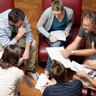 Eine Gruppe Personen sitzt zusammen und bespricht etwas, alle halten Notizen in den Händen.